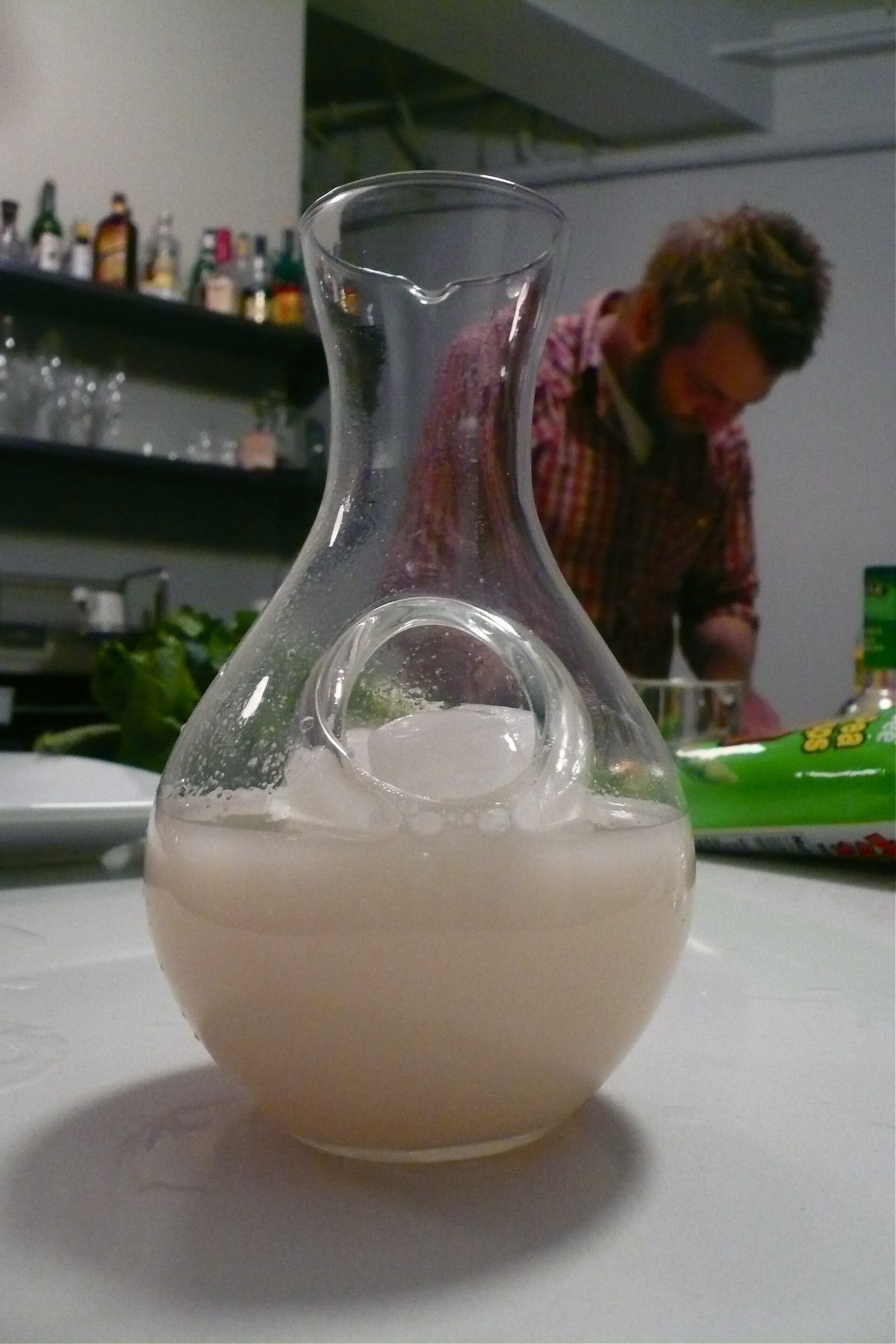 A glass carafe of cloudy sake chilling in a bed of ice on a bar