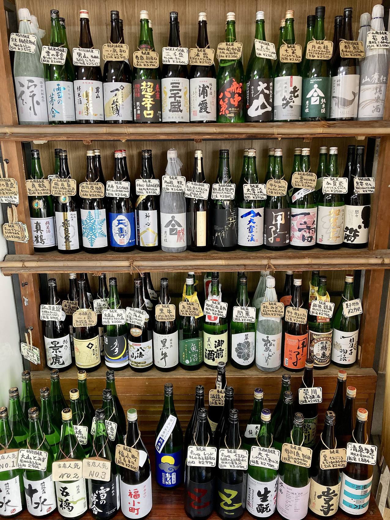 Shelves packed with labelled sake bottles, price tags hanging from each neck