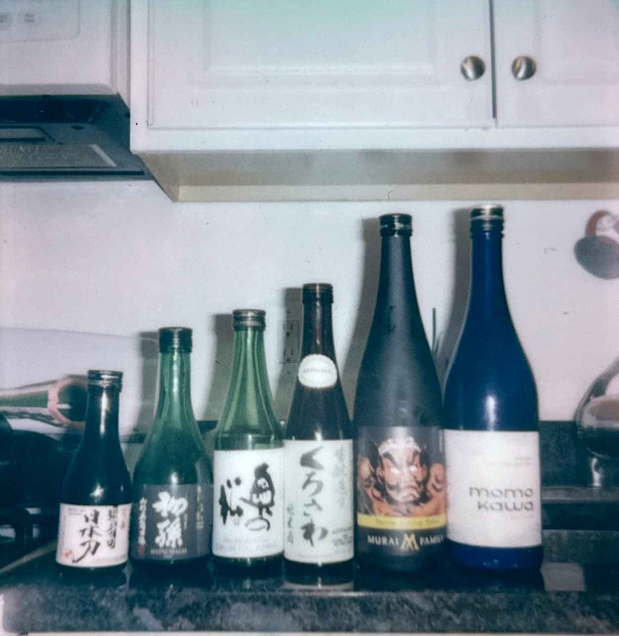 Six sake bottles lined up on a kitchen counter before the June 12 blind tasting